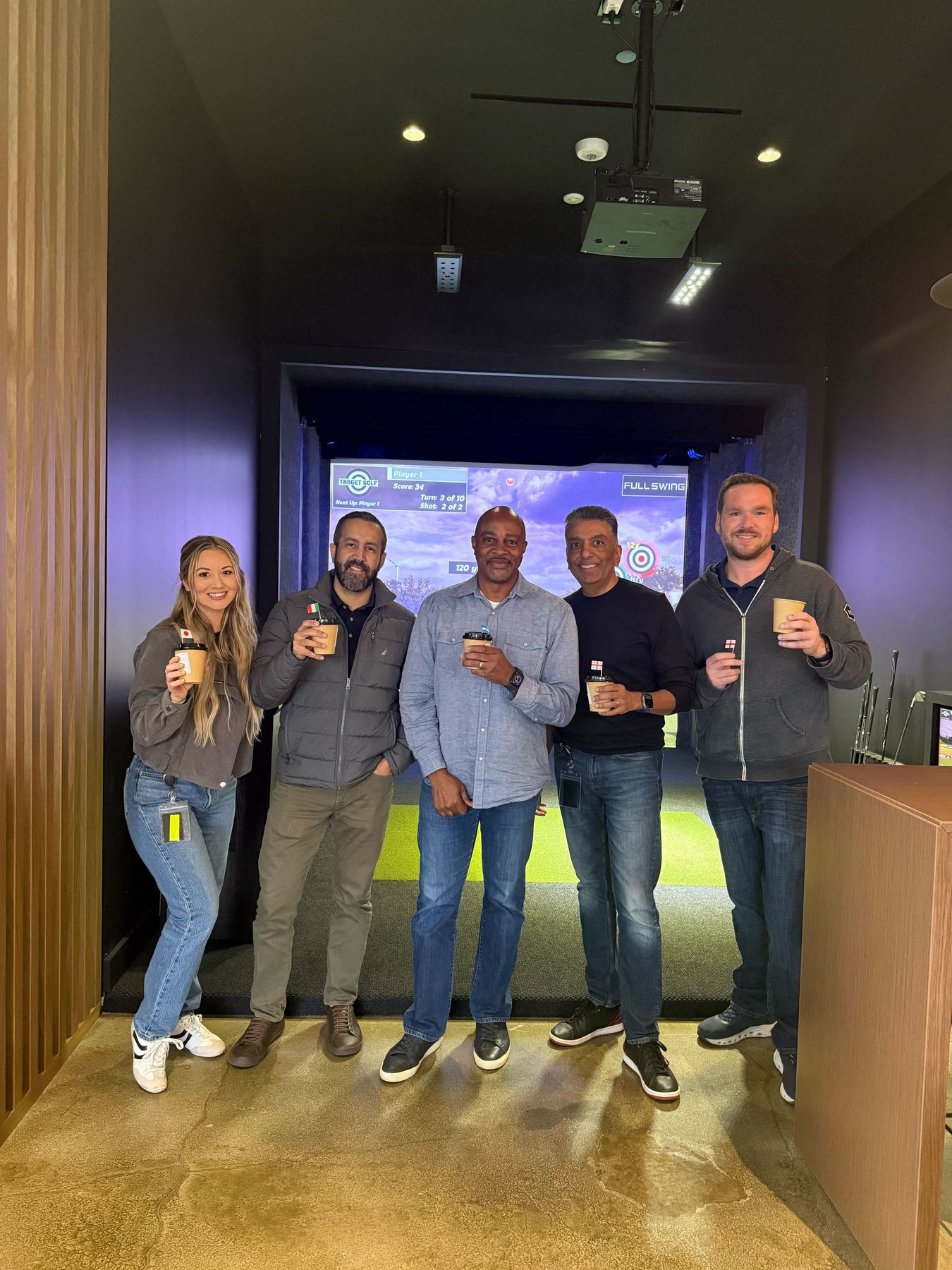 Golden Pet Brands team members on a golf simulator outing, holding coffee